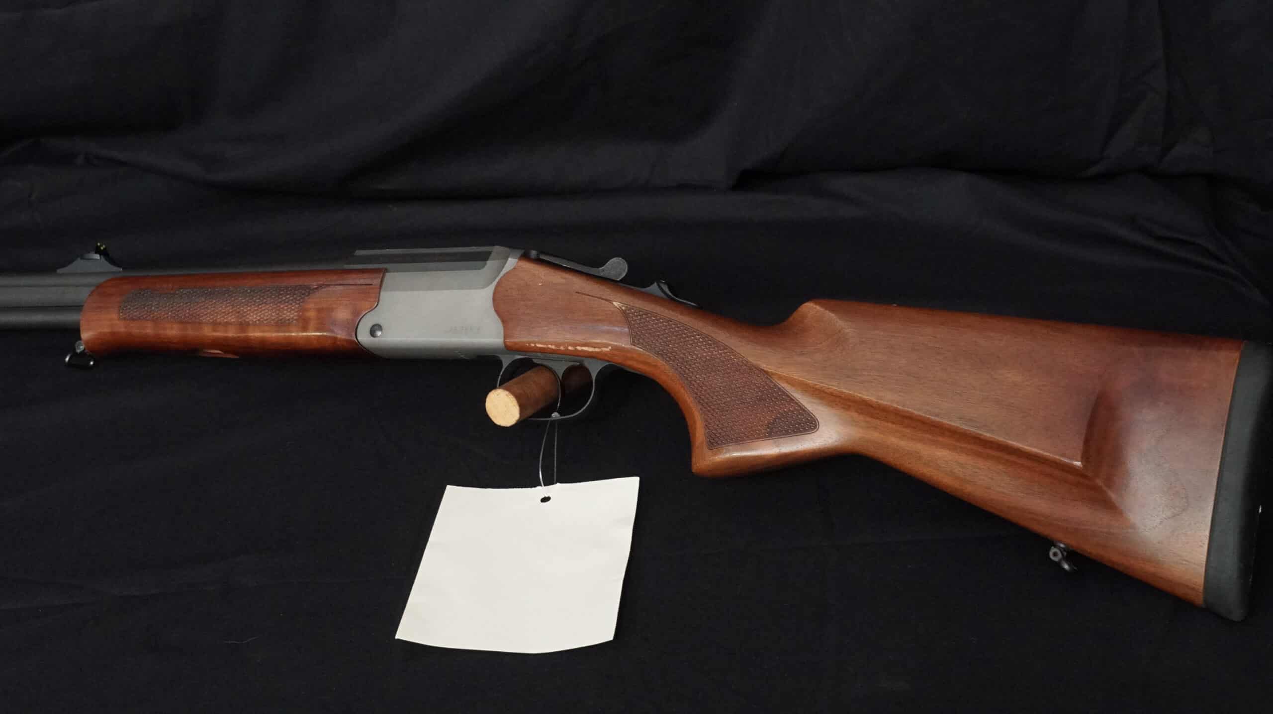 Carabine juxtaposée en bois brun avec détente simple et levier d'armement, posée sur un fond noir avec étiquette blanche.