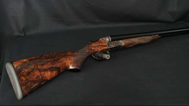 Fusil superposé élégant avec crosse en ronce de noyer foncé et récepteur en acier ouvragé, sur fond noir uni.
