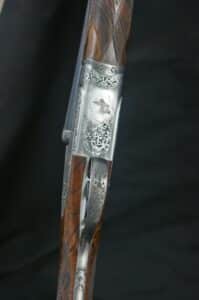 Fusil de chasse Piotti : boîtier argenté gravé d'un canard, rinceaux et monogramme. Crosse en bois veiné. Détail luxe.