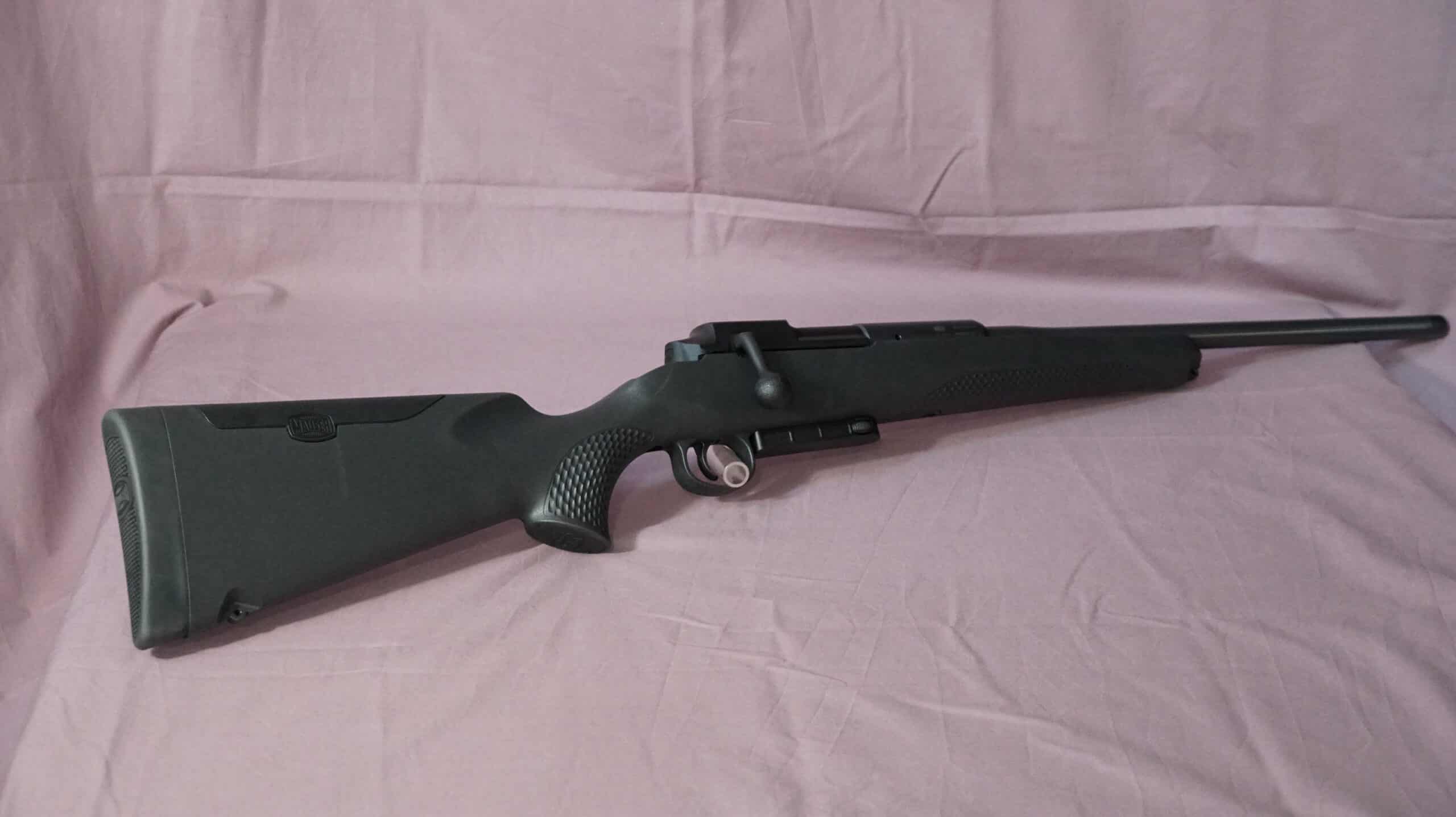 Fusil de chasse noir Savage avec crosse synthétique et loquet de sécurité visible, posé sur un tissu froissé rose-mauve.