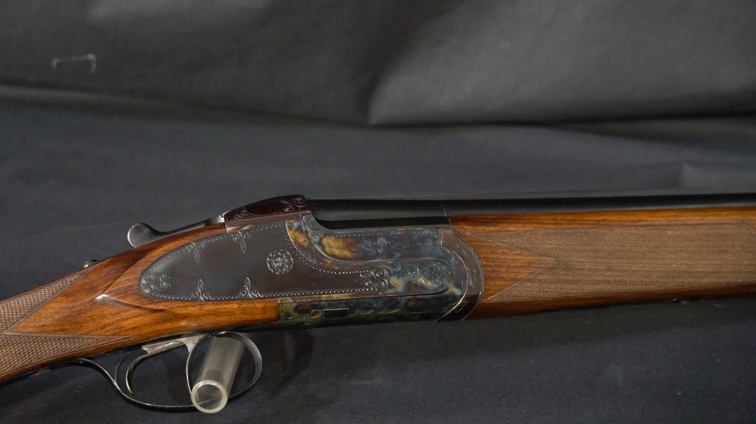 Détail d'une crosse de fusil juxtaposé en bois fin avec gravures florales sur la platine et détente.