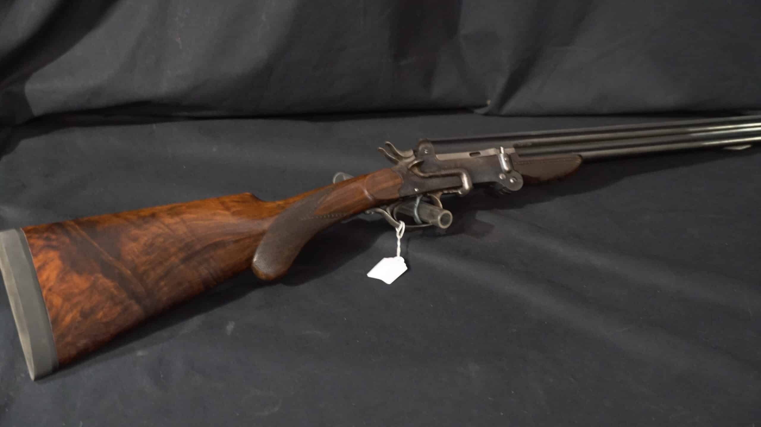 Fusil de chasse double à chiens extérieurs. Crosse en noyer figuré richement quadrillée, métal foncé. Étiquette d'inventaire blanche visible.