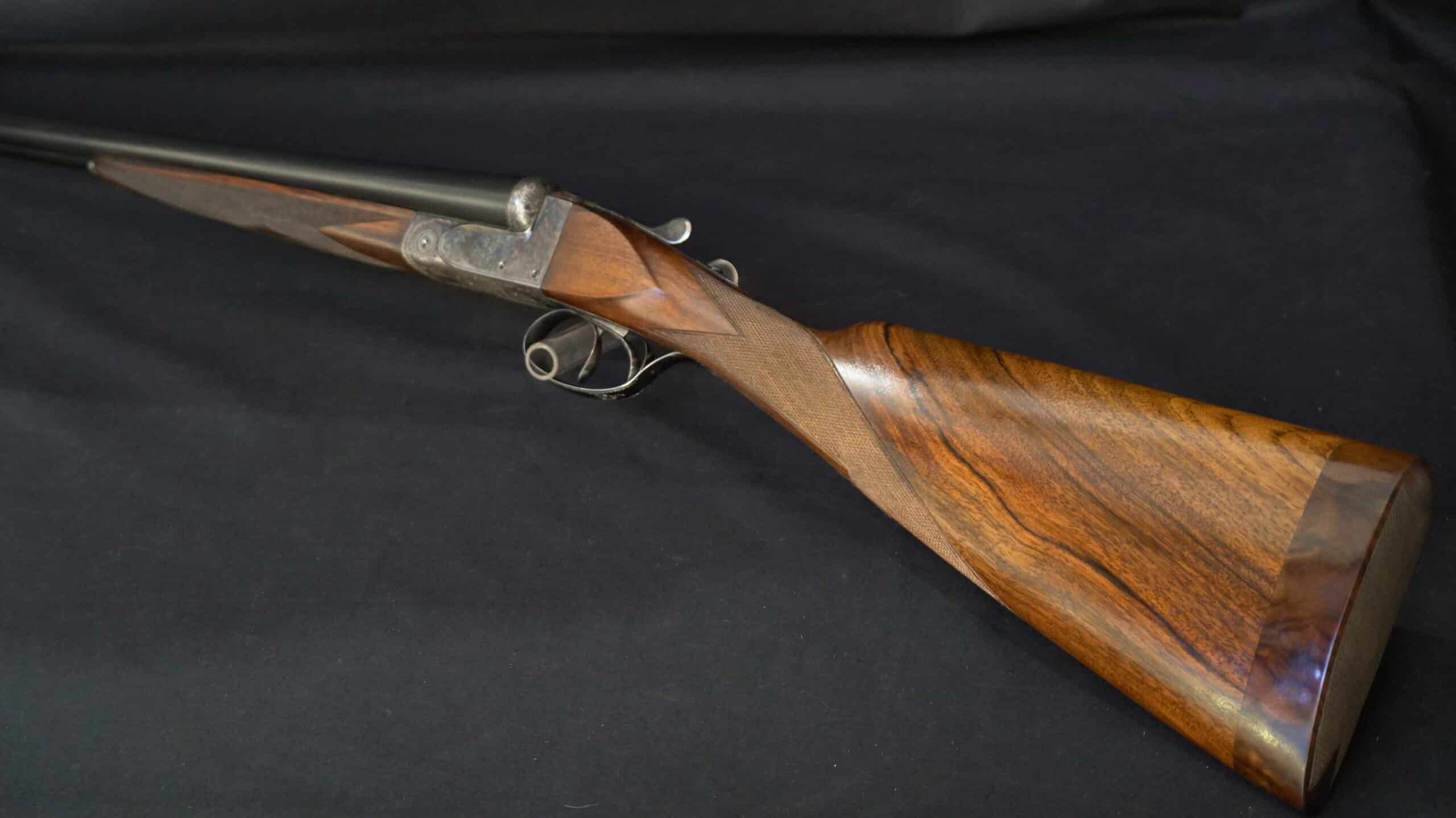Fusil de chasse juxtaposé avec crosse en noyer poli et boîtier de culasse gravé sur fond noir.