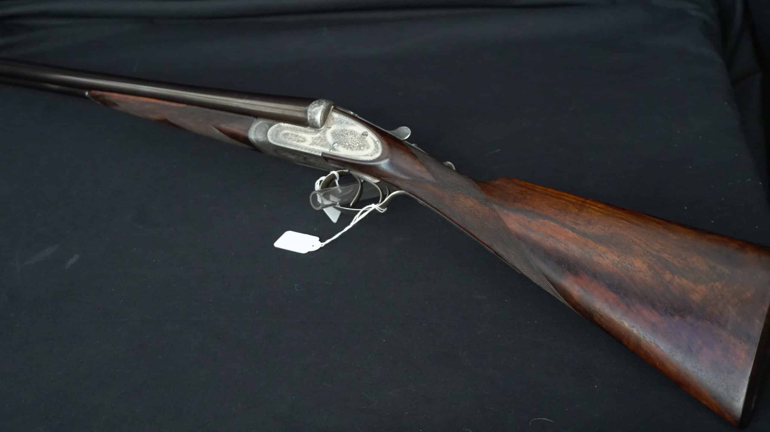 Fusil de chasse de luxe à platines, canons juxtaposés, crosse noyer quadrillée et fines gravures artisanales.