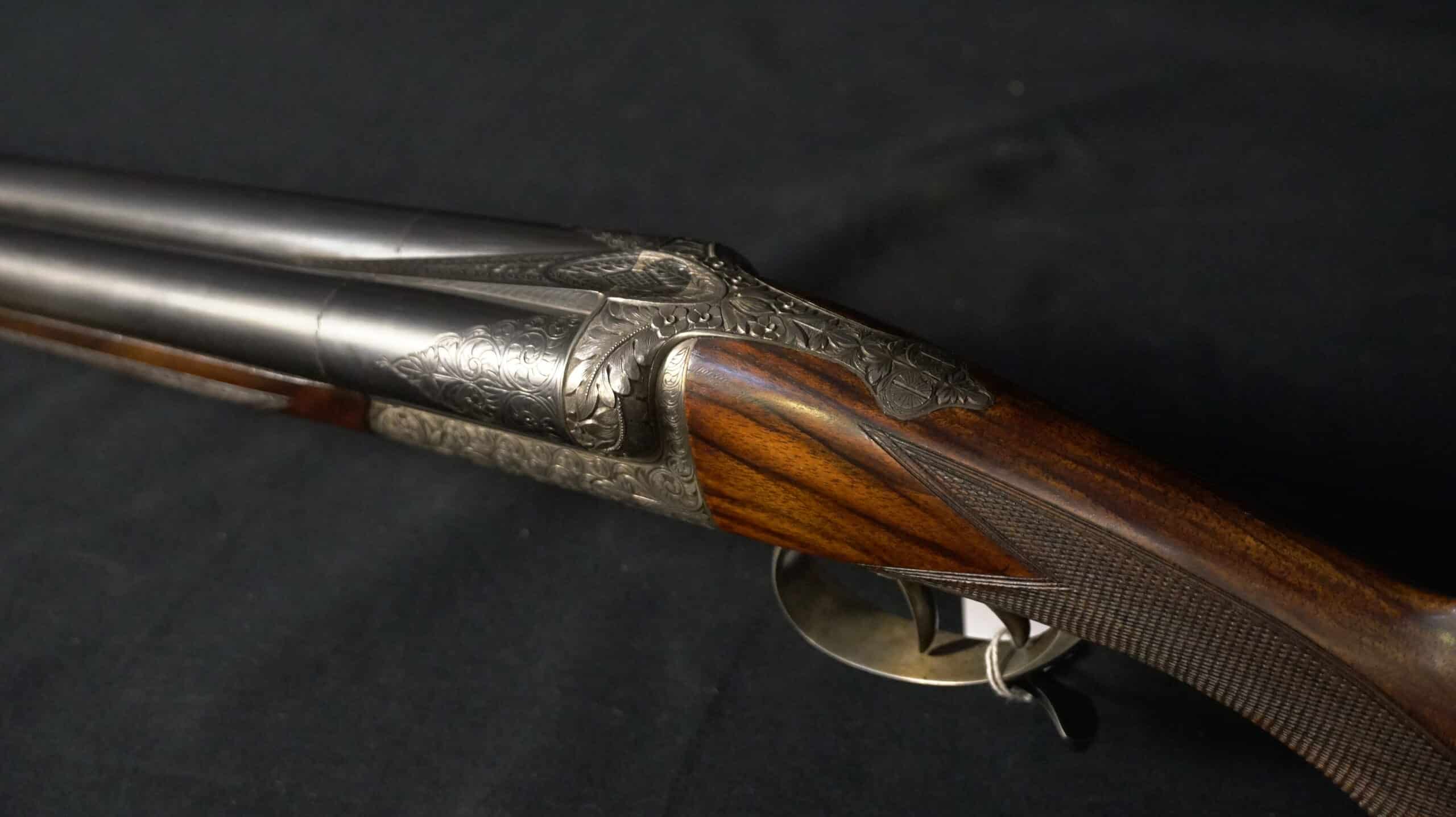 Fusil de chasse juxtaposé avec gravures artisanales sur la bascule et crosse en bois précieux quadrillée.