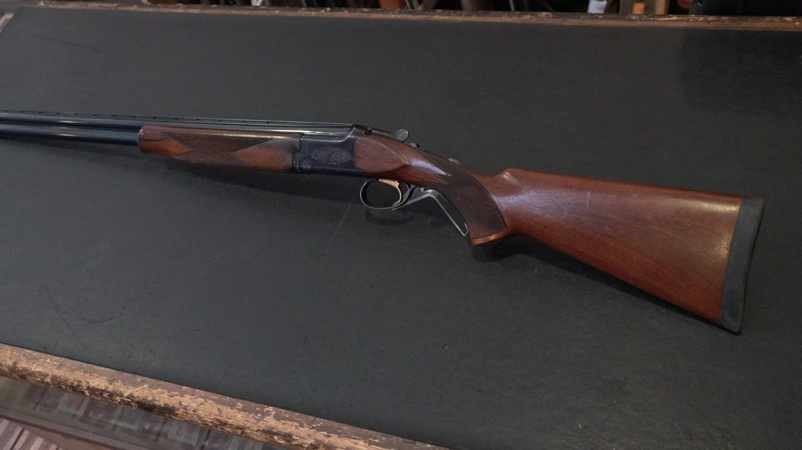 Fusil de chasse superposé avec crosse en bois et boîtier gravé sur fond sombre.