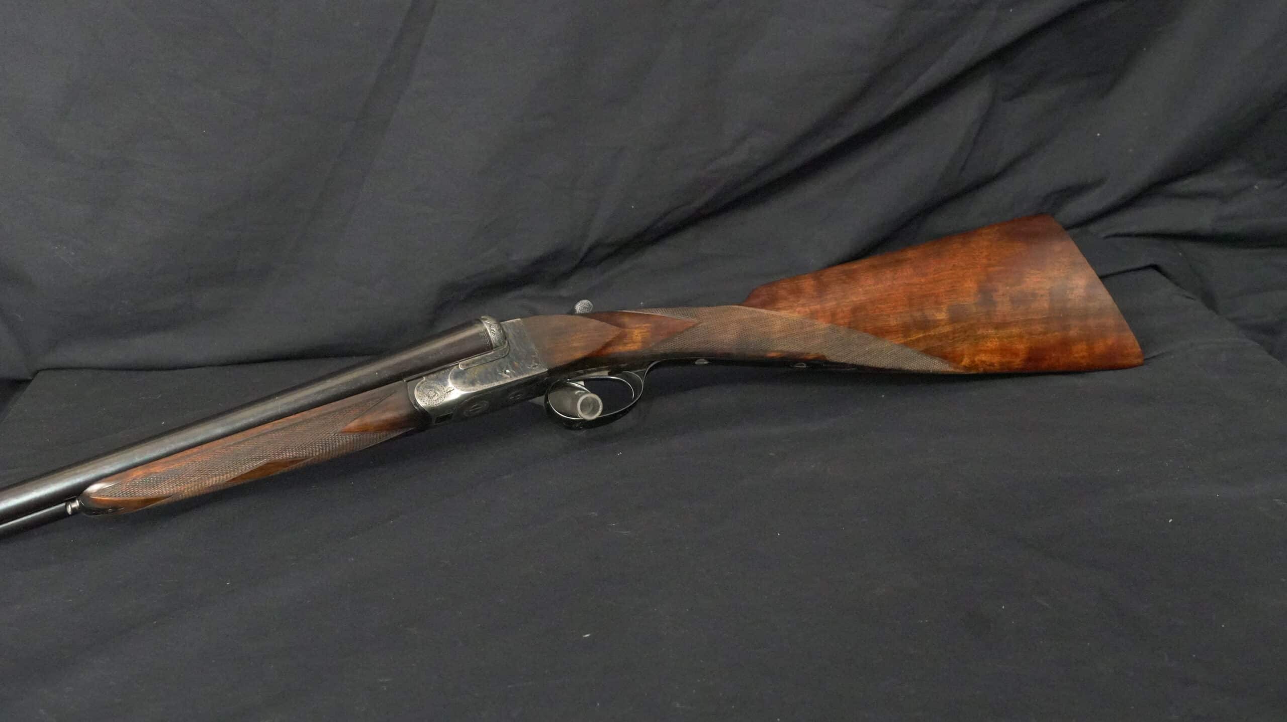 Fusil juxtaposé, crosse bois vernie et bascule gravée sur fond noir.