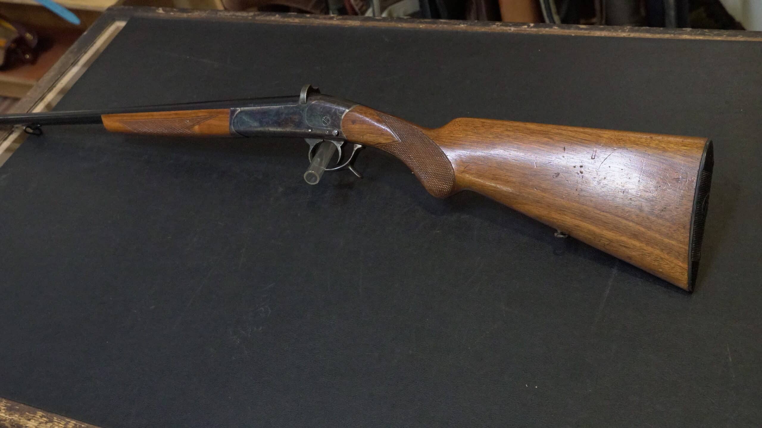 Fusil de chasse monocoup, crosse en bois de noyer quadrillée et boîtier jaspé sur tapis noir.