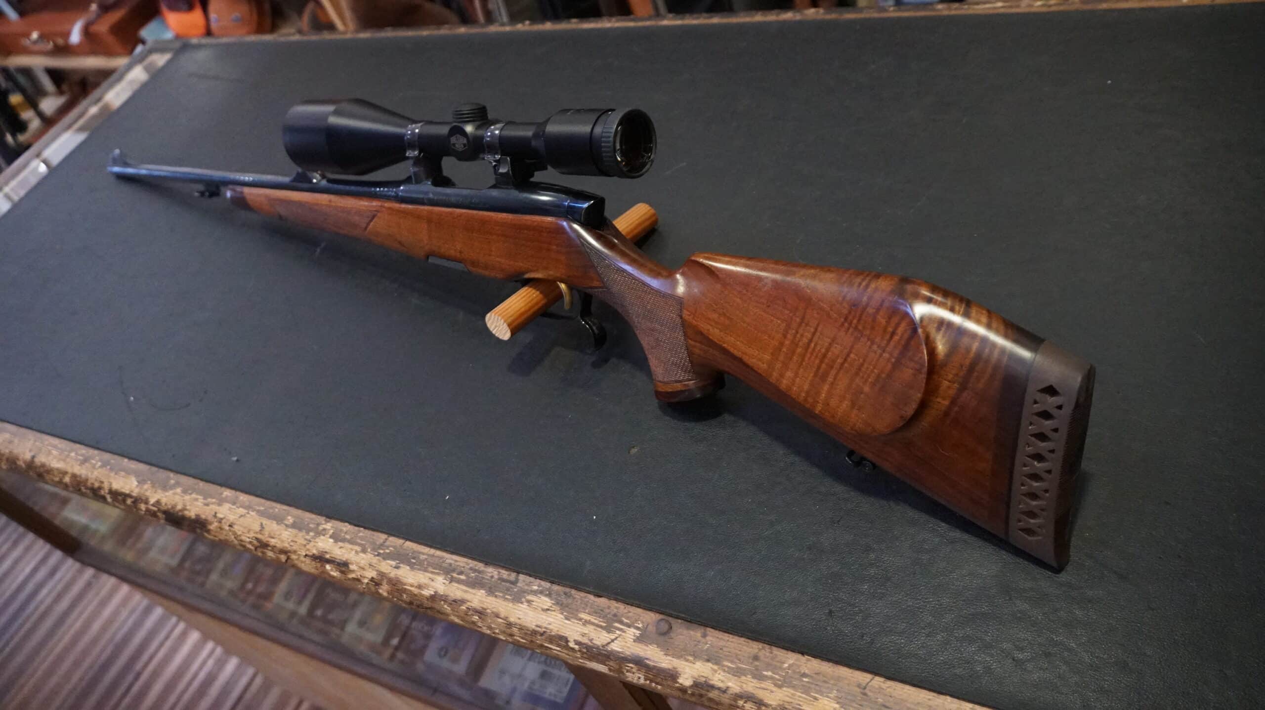 Carabine de chasse à verrou avec crosse en noyer sculptée et lunette de visée posée sur un support.