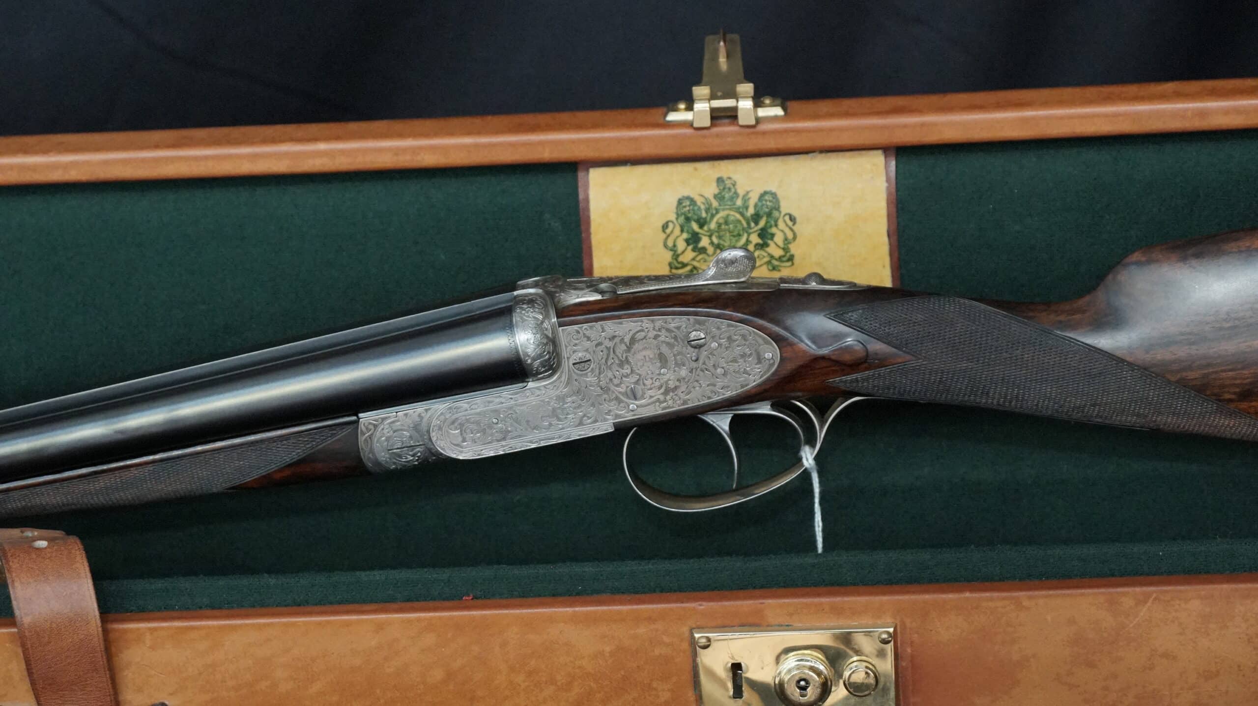 Fusil de chasse juxtaposé aux gravures fines dans son coffret de luxe doublé de vert avec blason.