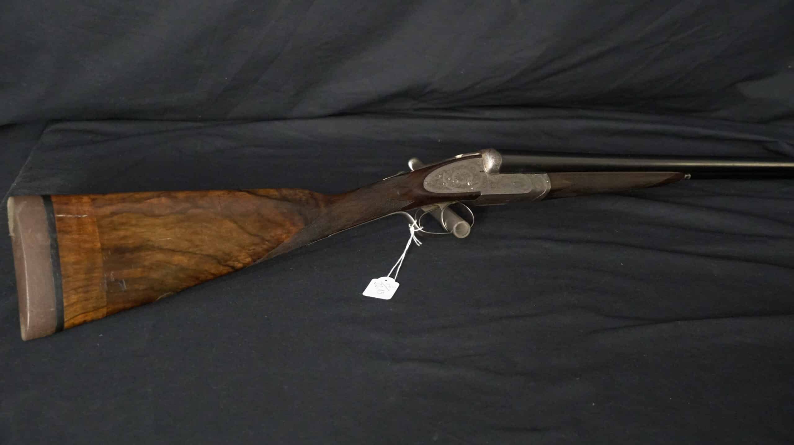 Fusil de chasse juxtaposé de luxe avec crosse en bois verni et gravures détaillées sur la culasse.