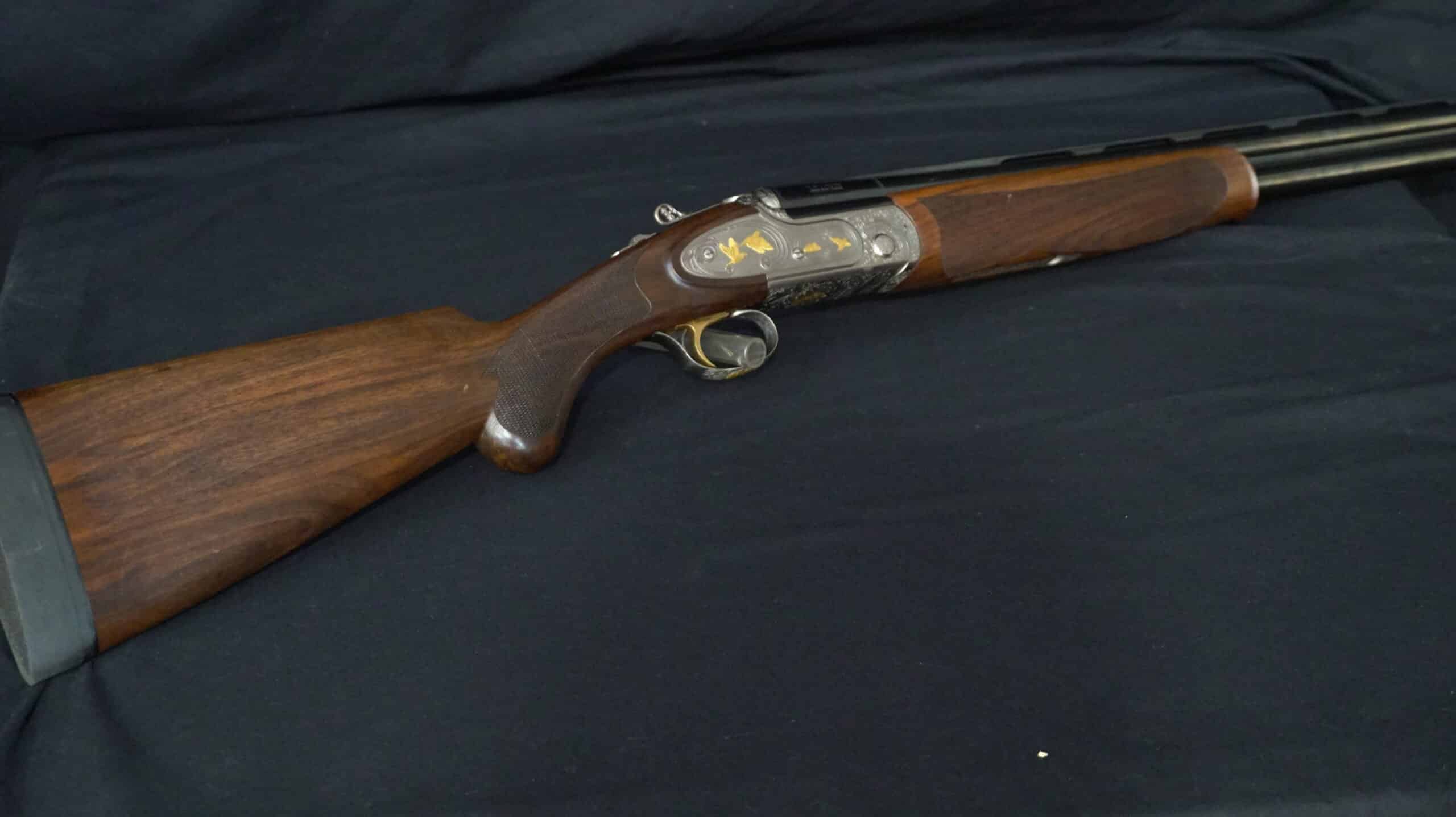 Fusil de chasse superposé de luxe avec gravures dorées de canards et crosse en bois sur fond noir.
